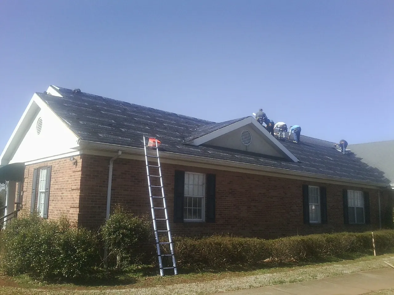 Crew tearing shingles off a brick ranch roof with a ladder set — Emergency Roof Repair work by our crew in Piqua