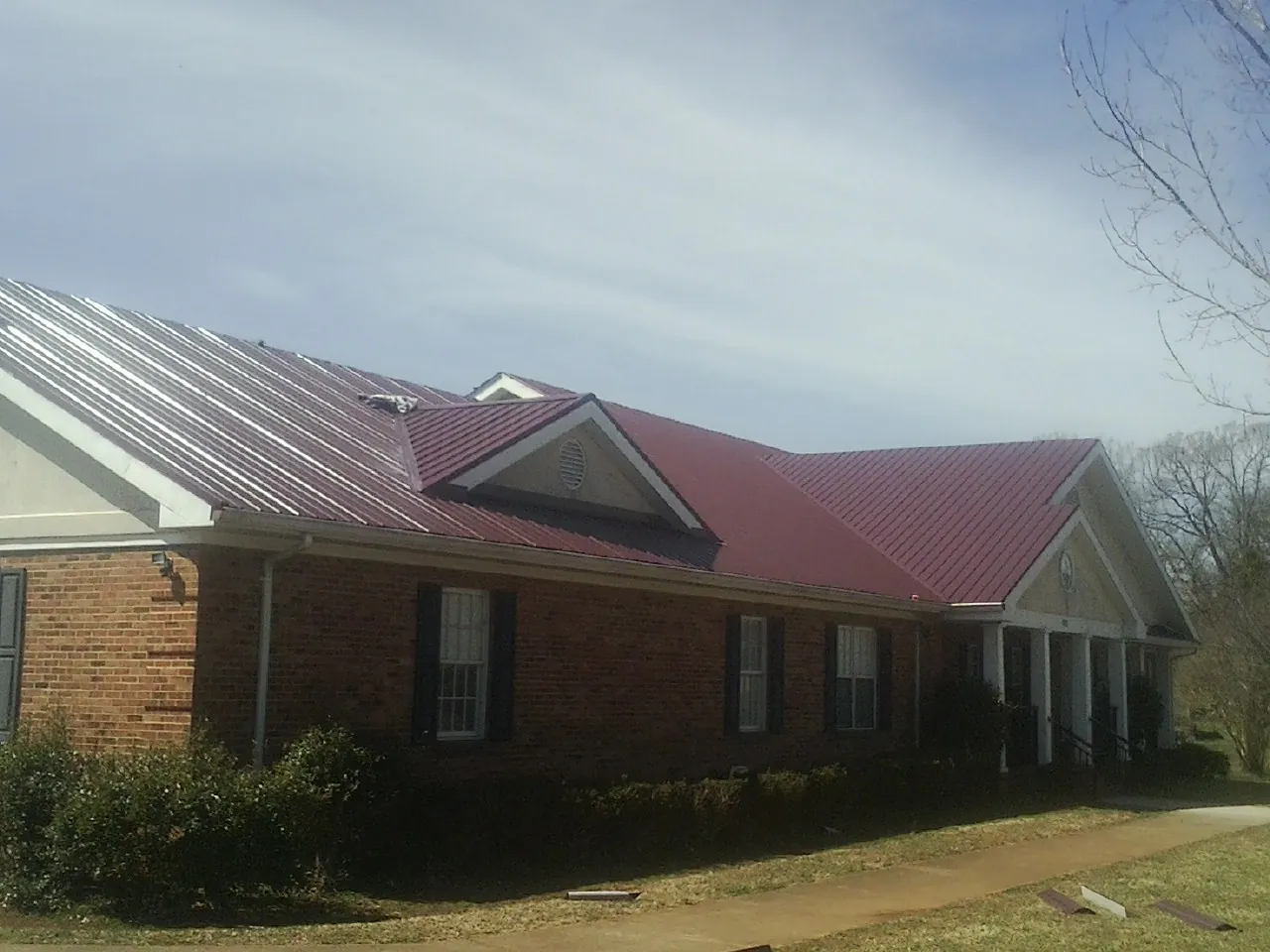 Red metal roof with gabled entries on a long brick building, from a Hail Damage Roof Repair job in Piqua