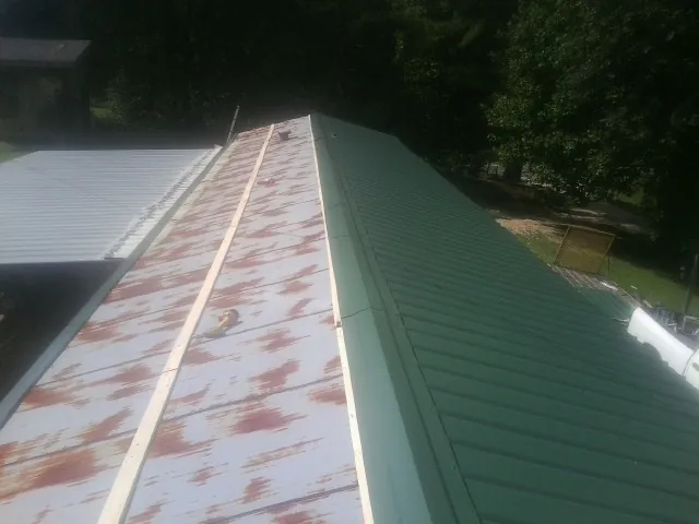 Old rusted panels beside newly installed green metal roofing — Wind Damage Roof Repair by Roofing Brothers in Piqua