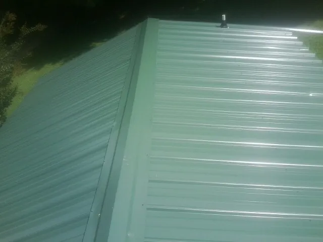 New green metal panels meeting at the ridge of a roof — Flat Roof Repair work by our crew in Piqua