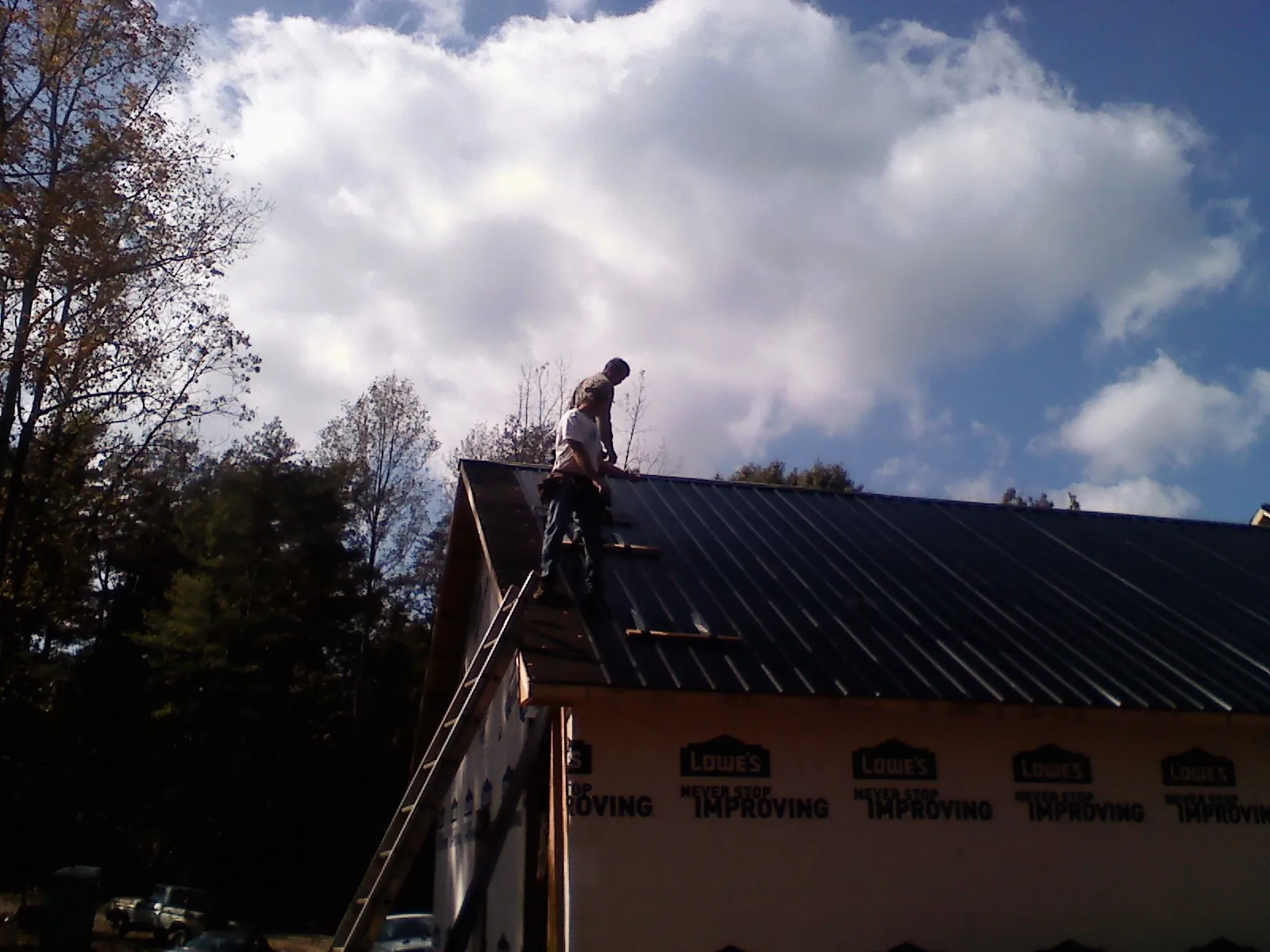 Roofer fastening dark metal panels high against a cloudy sky, from a Roof Inspection job in Piqua