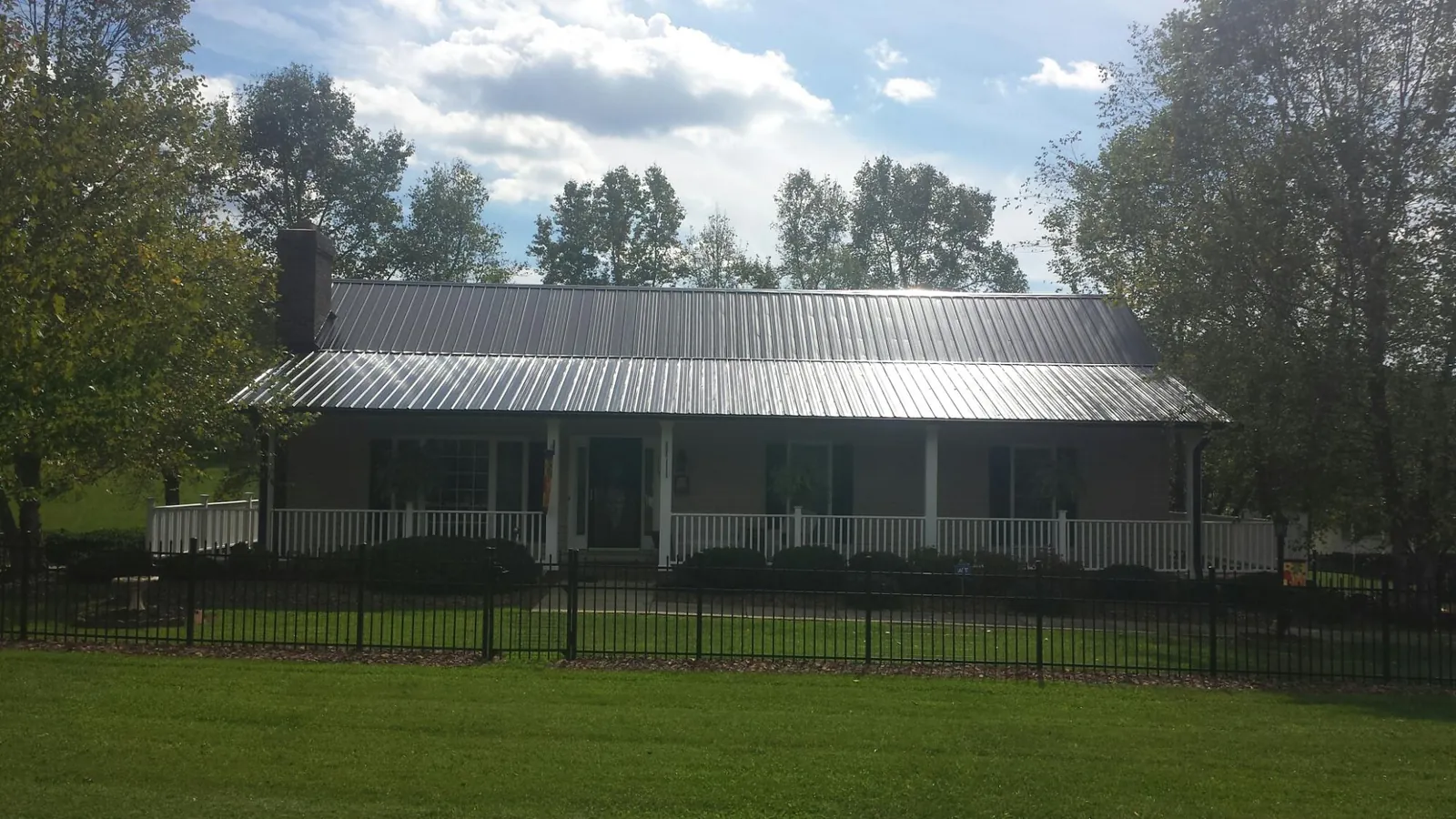 Gray metal roof on a brick ranch with a full width front porch — Gutter Guard Installation work by our crew in Piqua