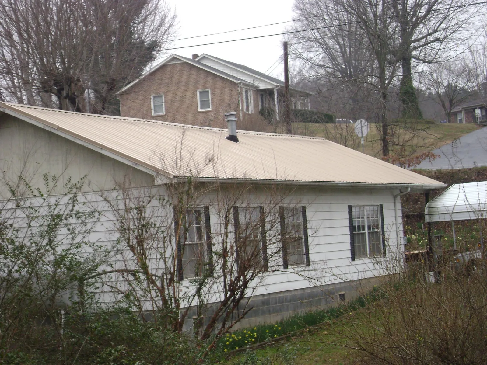 Tan metal roof on a white sided house set into a hillside — Commercial Roofing by Roofing Brothers in Piqua