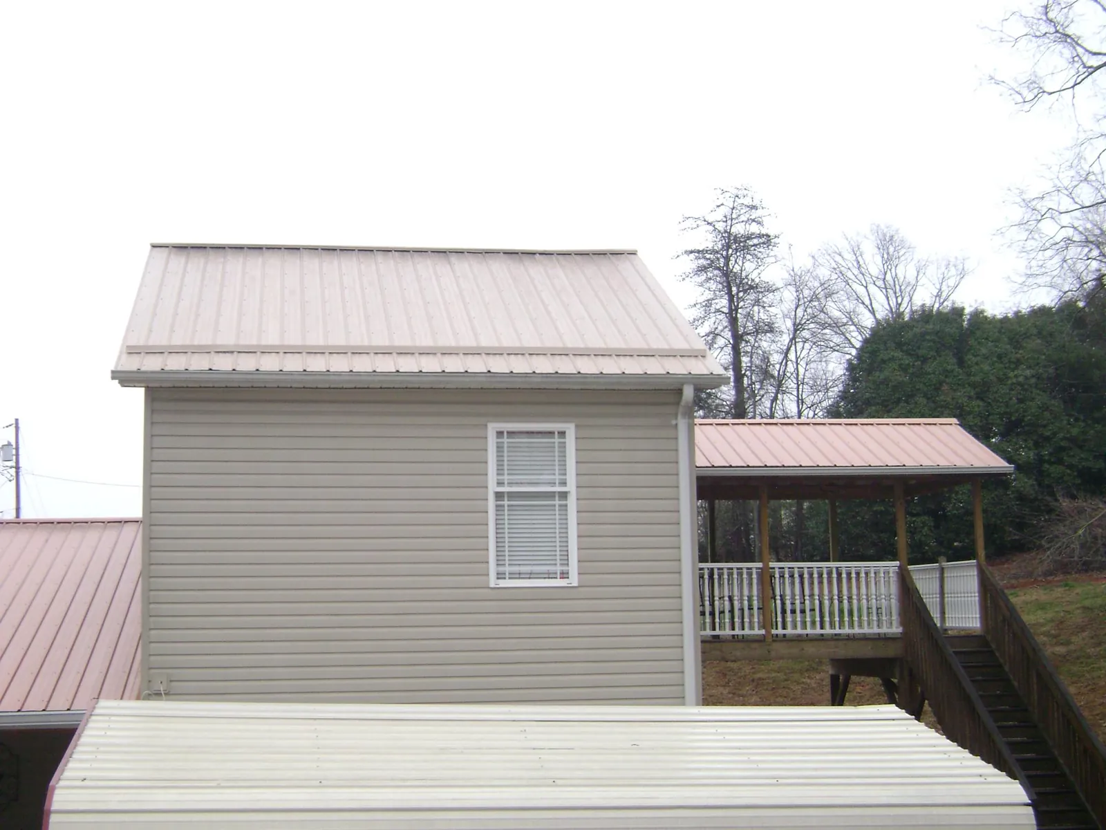Tan metal roofs on a two story addition and attached porch, from a Roof Replacement job in Piqua